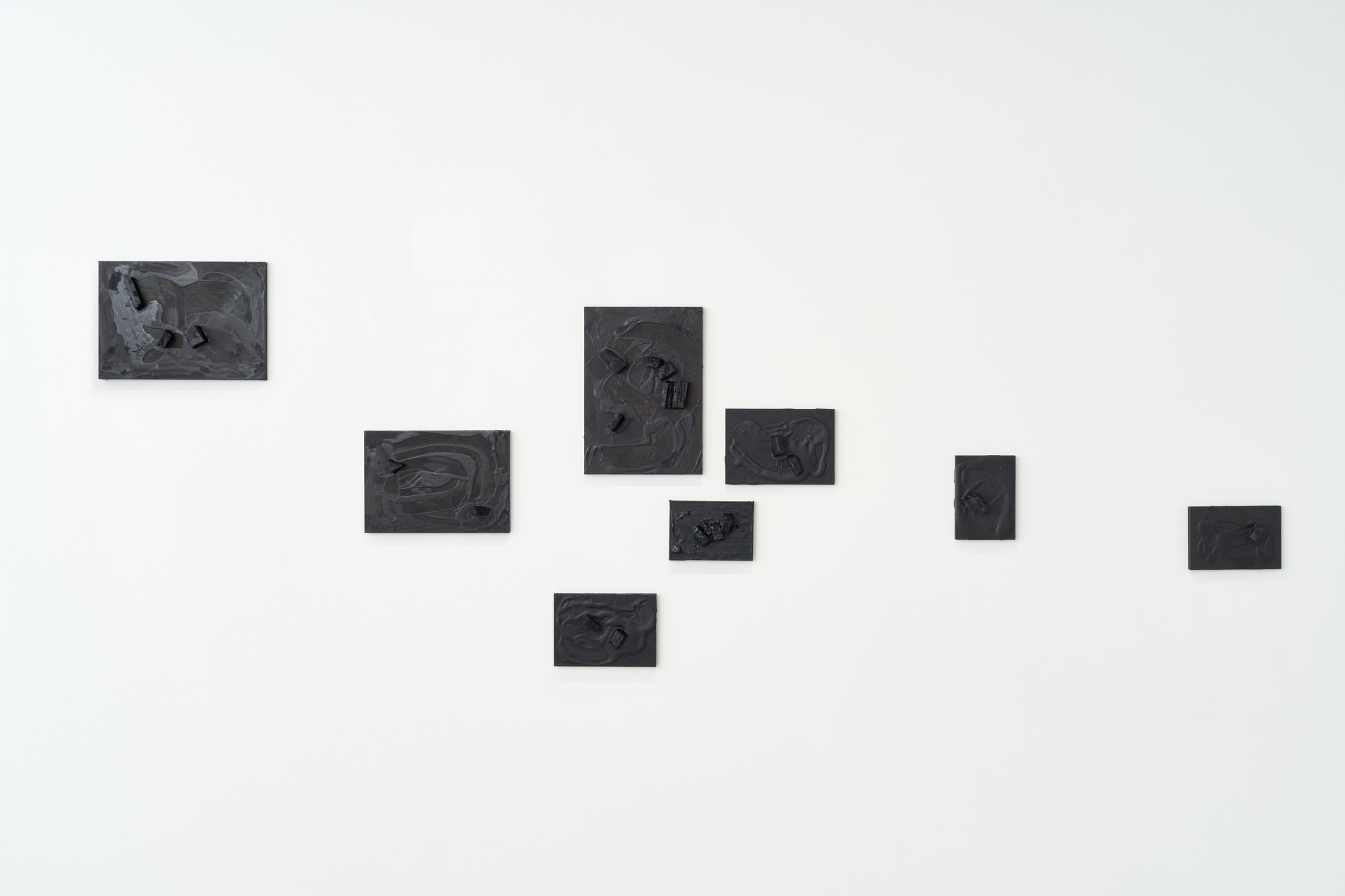The paintings hang as a scattered constellation across the wall, like wreckage seen from the air